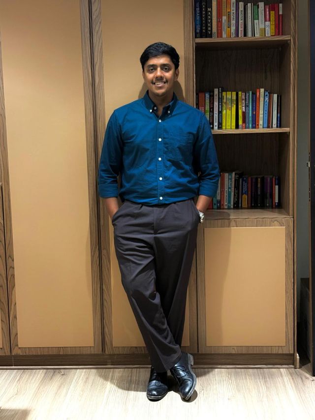 Usman in a blue shirt leaning beside a bookshelf